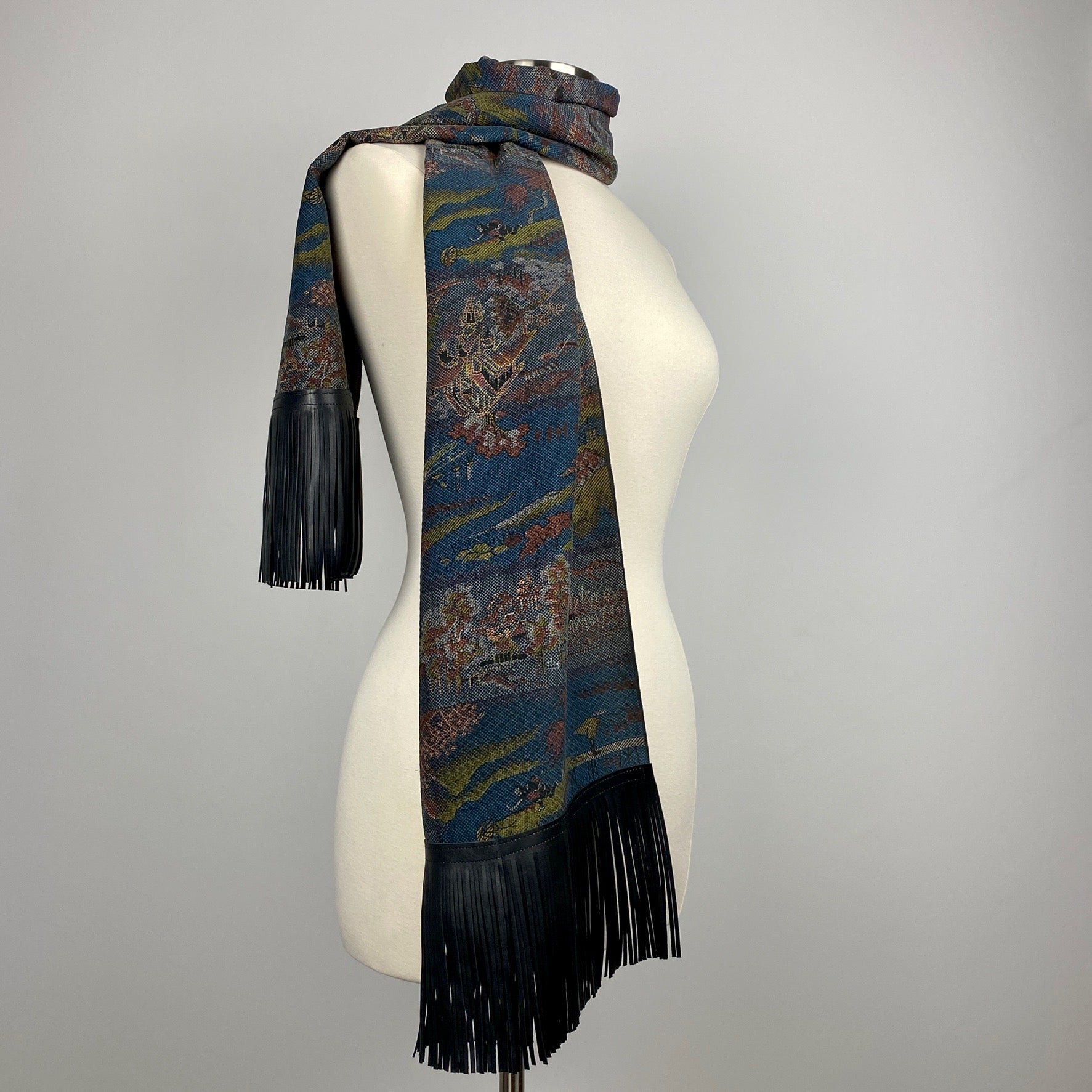 A dark blue kimono silk scarf with black leather fringe. Silk has scenery of people on a journey 