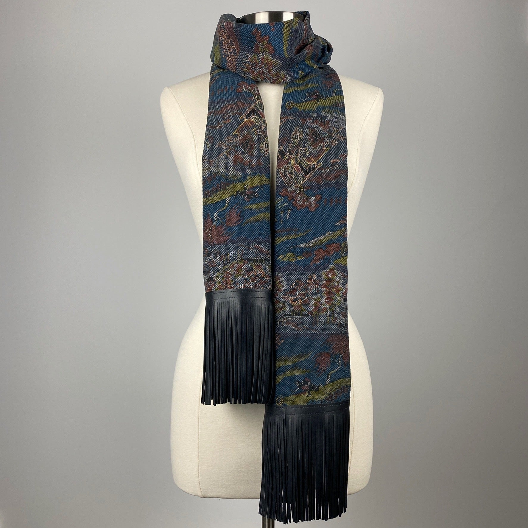 A dark blue kimono silk scarf with black leather fringe. Silk has scenery of people on a journey 